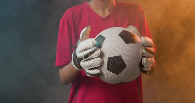 African American female keeper wearing red shirt white gloves holding ball, adjusting grip in haze