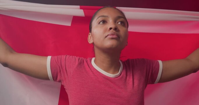 African American woman spreading and wrapping red-white flag, wearing red ringer tee, studio posing