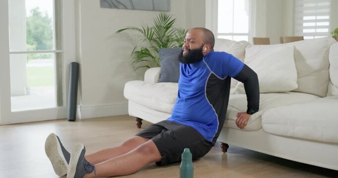 African American man grasping sofa edge, performing triceps dips for home workout in living room