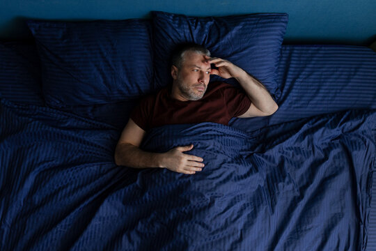 Man lying in bed holding head with hand, insomnia or stress concept