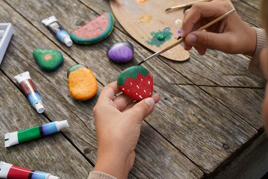 Process of painting fruits and vegetables on flat stones. A boy using brushes and colorful paints.