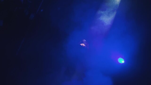 A cinematic top-down shot of a figure falling or floating through thick blue fog and spotlight. Surreal and abstract concept of gravity, mystery, or dreams.