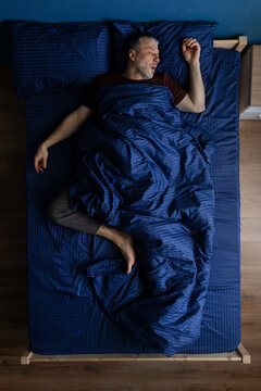 Top view of middle aged man sleeping in dynamic position across bed