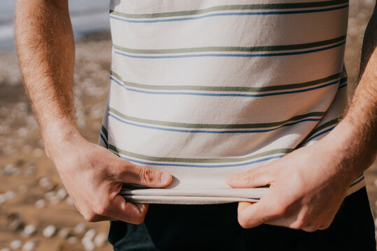 Man holds thin book on pebbled shore