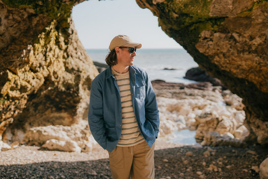 Man stands beneath rocky archway, gazing out to sea