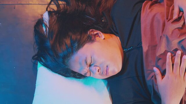 An intimate close-up of a woman lying down, tightly squeezing her eyes closed in apparent discomfort, pain, or emotional distress under artistic neon lighting.