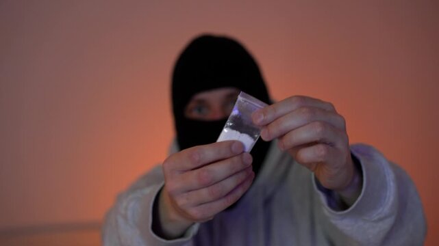 A masked man showing drugs and giving an up-turned gesture, illegal activity.
Police arrest a criminal in a black mask.