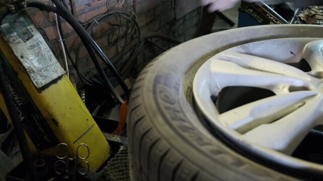 Car wheel and tire positioned on automotive repair equipment inside workshop. Alloy rim and rubber tire partially mounted on machine used for tire servicing. Vehicle maintenance, tire replacement