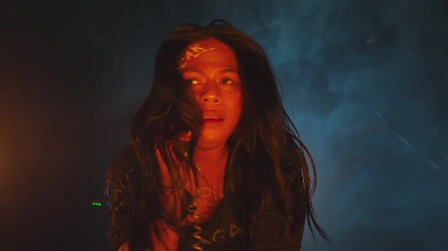 Dramatic close-up of a woman with words painted on her face yelling or crying into an old telephone receiver. Mixed blue and orange cinematic lighting creates high tension.