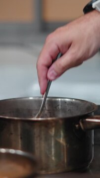 Chef cooking and stirring creamy sauce in a saucepan on a stove in a kitchen