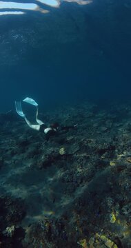 Woman with fins freediving underwater over coral reef with sun rays in Raja Ampat