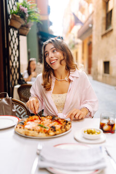 Portrait of a woman at a table on a restaurant terrace, eating hot pizza. A happy woman enjoys Italian pizza outdoors. Concept of food, relaxation, and weekends.