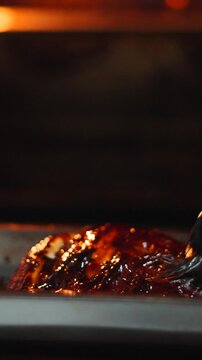 Chef brushing barbecue sauce on pork ribs cooking in the oven close up
