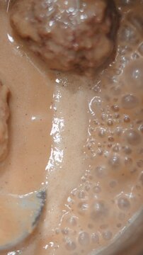 Chef stirring traditional swedish meatballs simmering in creamy sauce close up