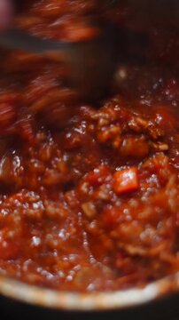 Close up view of a person stirring a steaming, rich bolognese sauce cooking in a pot