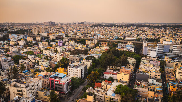 Aerial view of Bangalore city, Karnataka, India, showing a vast urban landscape with dense residential neighborhoods, modern development, and a lake surrounded by the expanding metropolis.