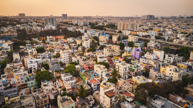 Aerial view of Bangalore city, Karnataka, India, showing a vast urban landscape with dense residential neighborhoods, modern development, and a lake surrounded by the expanding metropolis.