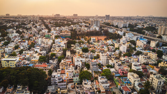 Aerial view of Bangalore city, Karnataka, India, showing a vast urban landscape with dense residential neighborhoods, modern development, and a lake surrounded by the expanding metropolis.