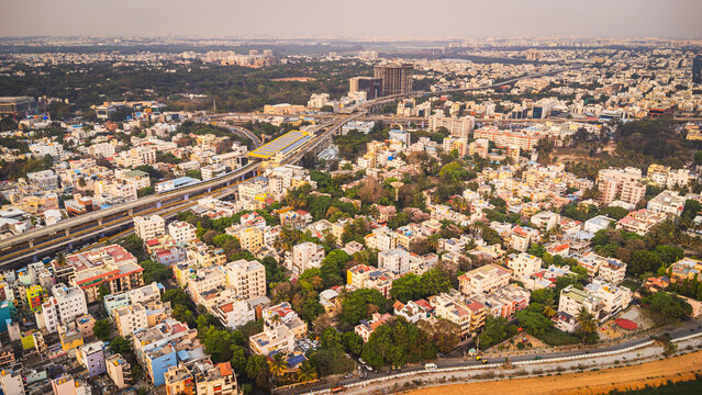 Aerial view of Bangalore city, Karnataka, India, showing a vast urban landscape with dense residential neighborhoods, modern development, and a lake surrounded by the expanding metropolis.