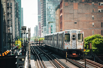 Naklejka premium Train of public transportation arriving on elevated railway above busy street in downtown Chicago. Urban transport, city life, infrastructure, and daily commute concept.