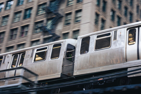 Train of public transportation on the move on elevated railway above street in downtown Chicago. Urban transport, city life, infrastructure, and daily commute concept.