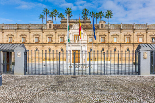 Seville, Spain - Feb 13, 2020: Mannerist facade of the Parliament of Andalusia building seen behind a black iron fence under a bright blue sky, showcasing historic regional government heritage.