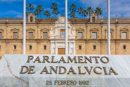 Seville, Spain - Feb 13, 2020: Renaissance facade of the Parliament of Andalusia, formerly Hospital de las Cinco Llagas, with marble signage and national flags on a sunny winter day in the city.
