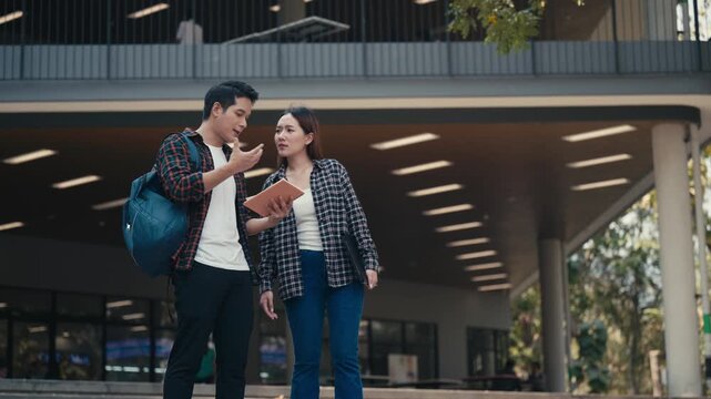 Young man and woman standing together outside a university building. Male student explaining something on a digital tablet to his female classmate
