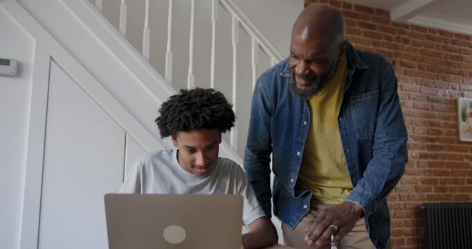 Father and Teenage Son Engaged in Learning on Laptop at Kitchen Table