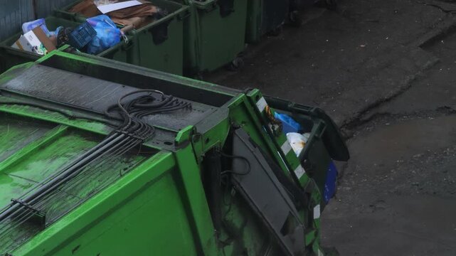 Garbage truck working in a residential yard, collecting waste from containers and compacting it. Aerial view shows a sanitation worker loading trash using the automatic bin lifting mechanism