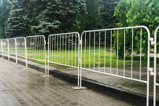Temporary street fencing installed near a curb on a rainy day with lush trees and wet pavement in the background.