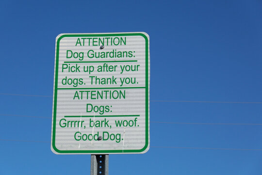Rectangular sign with green text on a white background. It says, "ATTENTION Dog Guardians: Pick up after your dogs. Thank you. ATTENTION Dogs: Grrrrr, bark, woof. Good Dog." 