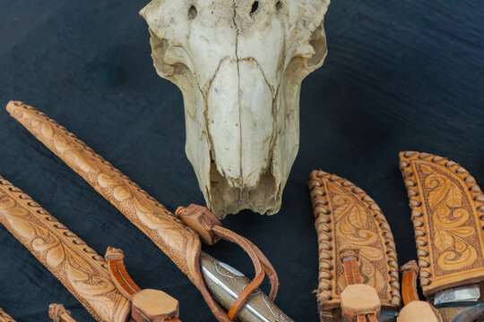 Animal skull with handmade leather knife sheaths and traditional carved details rustic composition close up