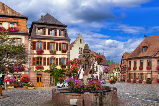 View of a square with fountain in Bergheim Alsace France. Historic town architecture and stone basin under cloudy sky