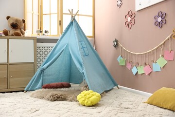 Colorful paper notes and beautiful decor hanging on beige wall near toy wigwam in stylish children's room. Interior design © New Africa
