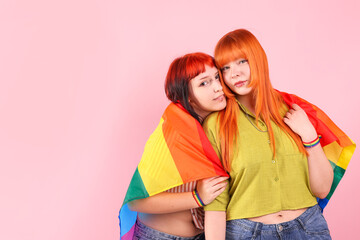 Lovely lesbian couple with rainbow flag on pink background, space for text. LGBT concept