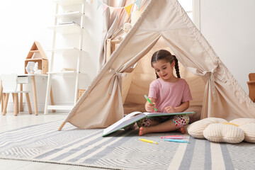 Little girl drawing in sketchbook near toy wigwam at home, space for text © New Africa