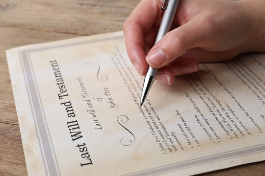 Woman signing Last Will and Testament at wooden table, closeup