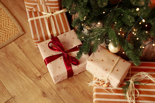 Present boxes placed under a Christmas tree with decorations and lights in a living room during holiday season