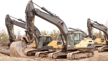 Rząd nowoczesnych koparek gąsienicowych stoi na placu budowy. Potężne, żółte maszyny z długimi ramionami są gotowe do robót ziemnych. W tle widać drzewa i błękitne niebo z delikatnymi chmurami © tomo81