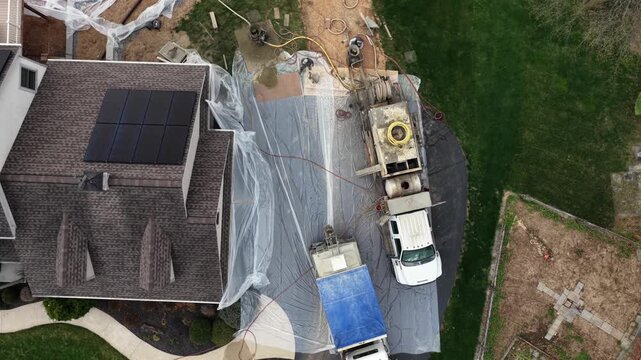 Top-down aerial view of construction site in suburban USA neighborhood, showing gunite truck parked beside house with solar panels during backyard pool installation work.