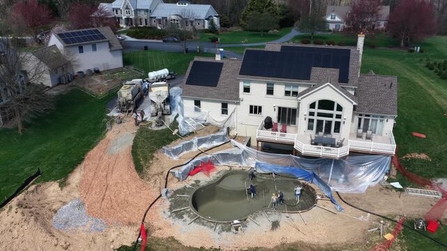 Aerial drone view of workers applying gunite to backyard swimming pool at suburban American home with solar panels, showing construction, teamwork and residential development. Top down.