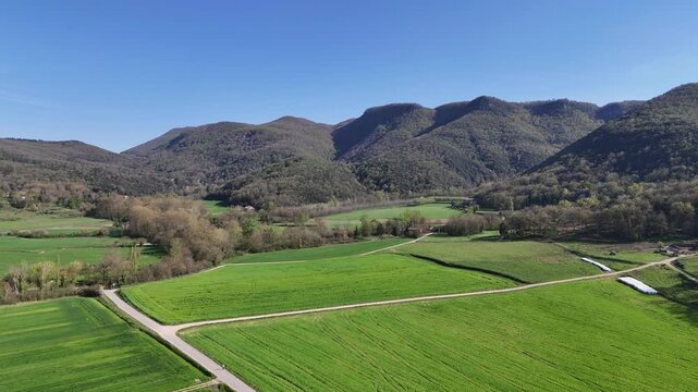 Drone flying over green fields and mountains in Vall d'en Bas, Spain