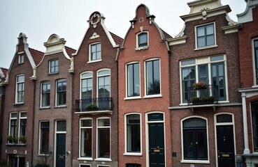 Fototapeta premium Row of traditional Dutch houses with stepped gables in Amsterdam. Red brick facades feature large windows and dark doors. Some balconies hold potted plants.