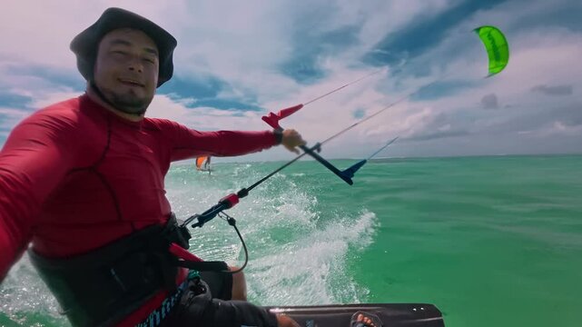 A male kitesurfer in a red sweater and sunhat films himself riding a huge ocean wave. Extreme sports