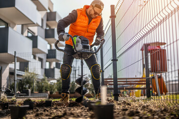 Gardener using tools hand-held soil hole drilling machine or portable manual cordless earth auger for prepare the soil for planting plants. © Peter