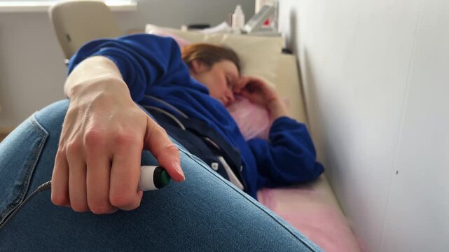 Expectant woman lying in a clinic bed during a medical examination, holding a fetal movement counter button while undergoing a non-stress test to monitor the baby's health