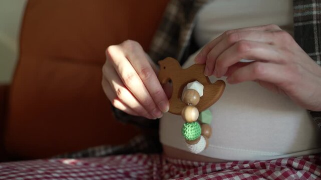 Close-up of a pregnant woman's hands holding a wooden baby teether toy in the shape of a horse, showcasing her baby bump while anticipating the arrival of her newborn child