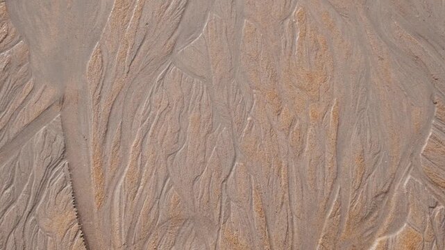 Abstract texture of wet sand with natural wave patterns on tropical beach in Phuket, Thailand. Minimalistic background with organic lines and earthy tones. Nature detail, texture