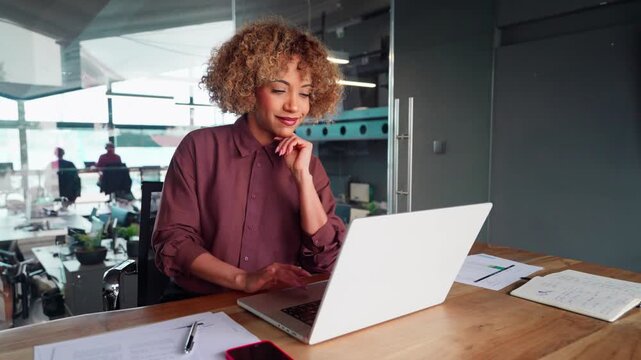 Middle-aged busy lAfrican American business woman working on laptop computer sitting in office. Young entrepreneur manager businesswoman using pc for communication, analysing and learning at workplace